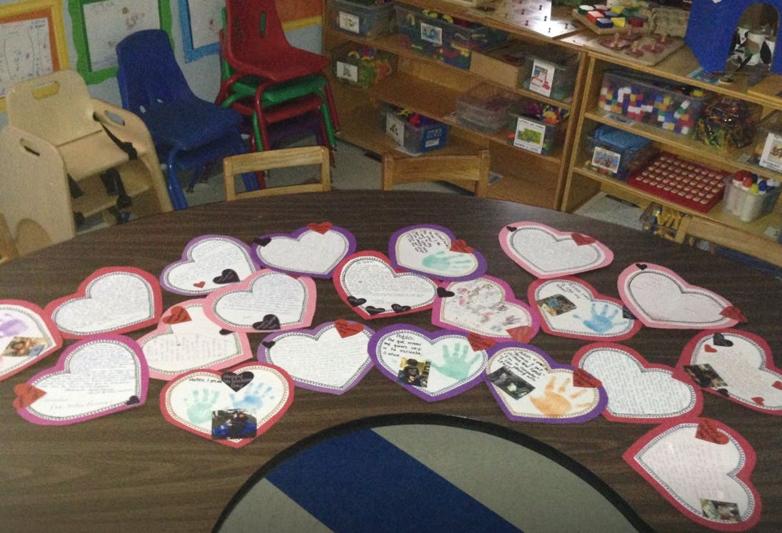 Heart-shaped crafts with handprints and drawings on a table in a classroom