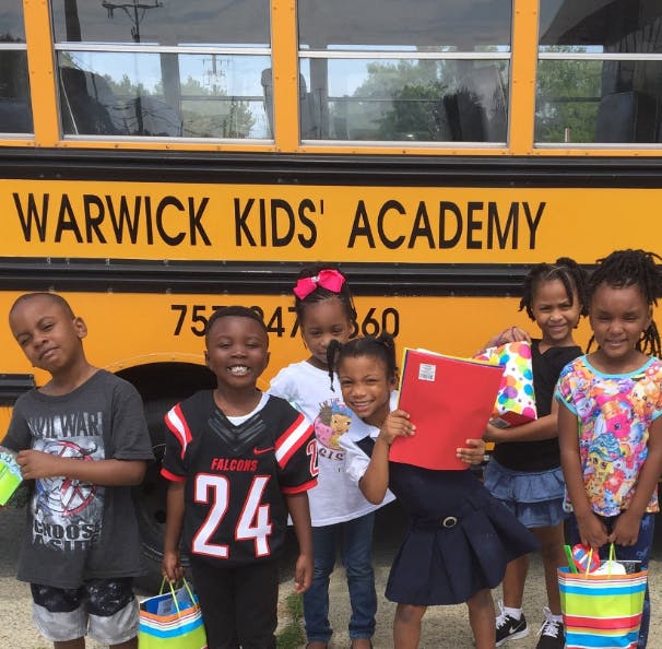 Children standing in front of a school bus with "WARWICK KIDS' ACADEMY" on it