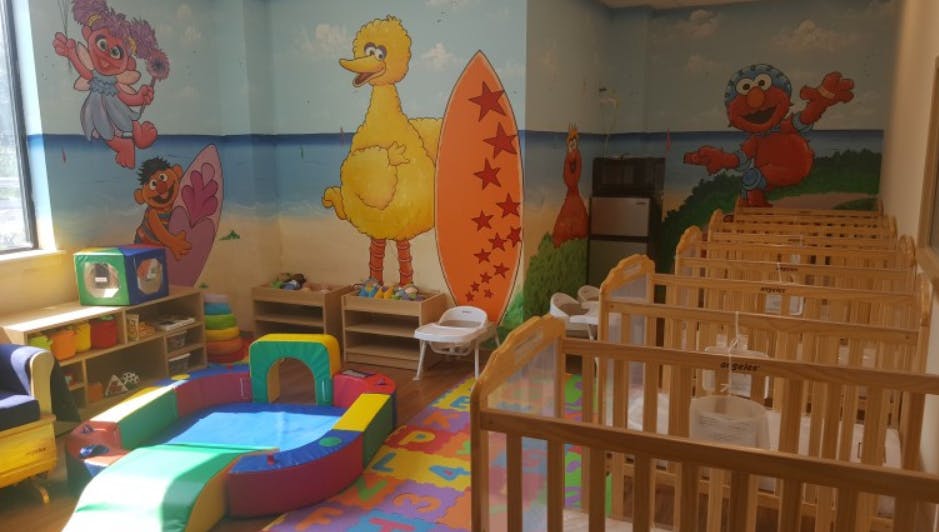 Playroom with colorful wall murals, soft play equipment, and cribs