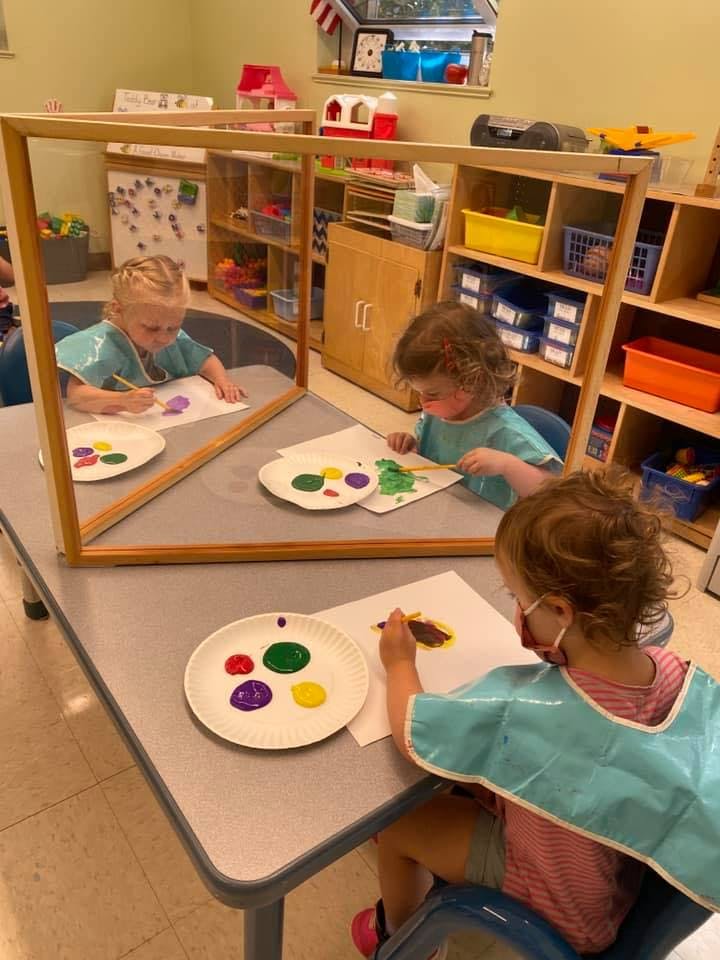 Three children painting at a table in a classroom