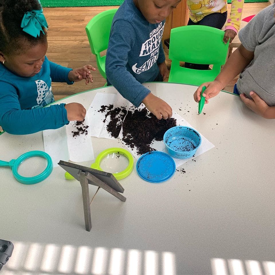 Children playing with dirt and magnifying glasses at a table