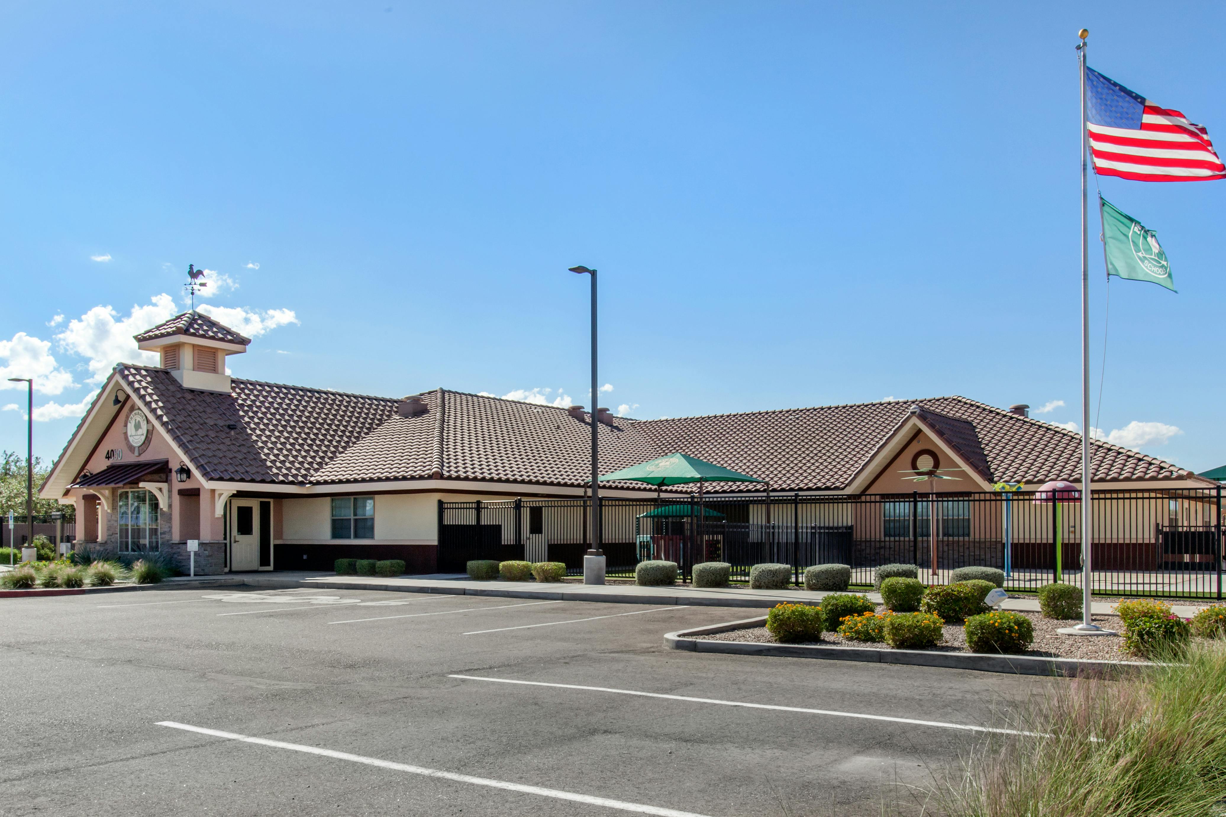 A low, sprawling building with a tile roof and a small tower, with a fenced play area