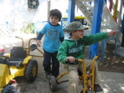 Two children with one riding a toy vehicle and another standing nearby