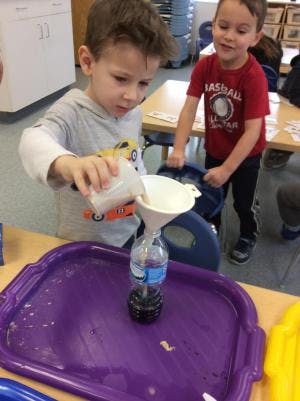 Child pouring liquid into a bottle through a funnel in a classroom