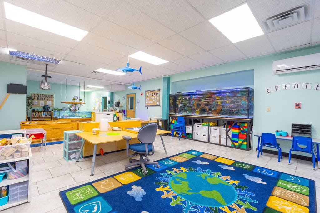 Classroom with a large fish tank, tables, chairs, and a world map rug