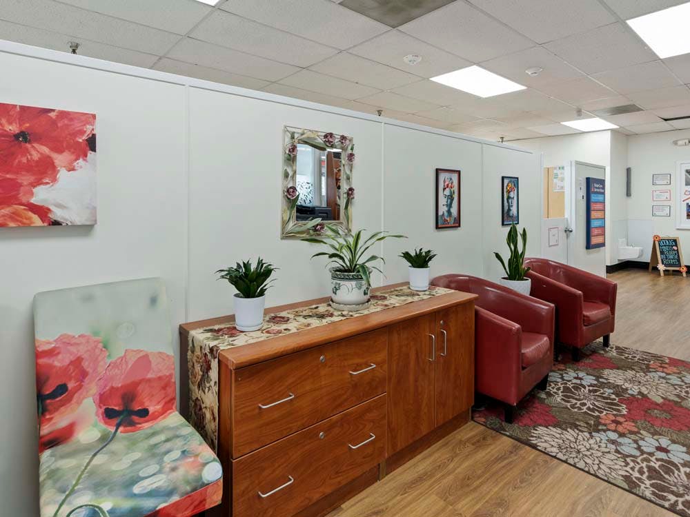 Lobby area with a wooden cabinet, red armchairs, a floral rug, and art on the walls