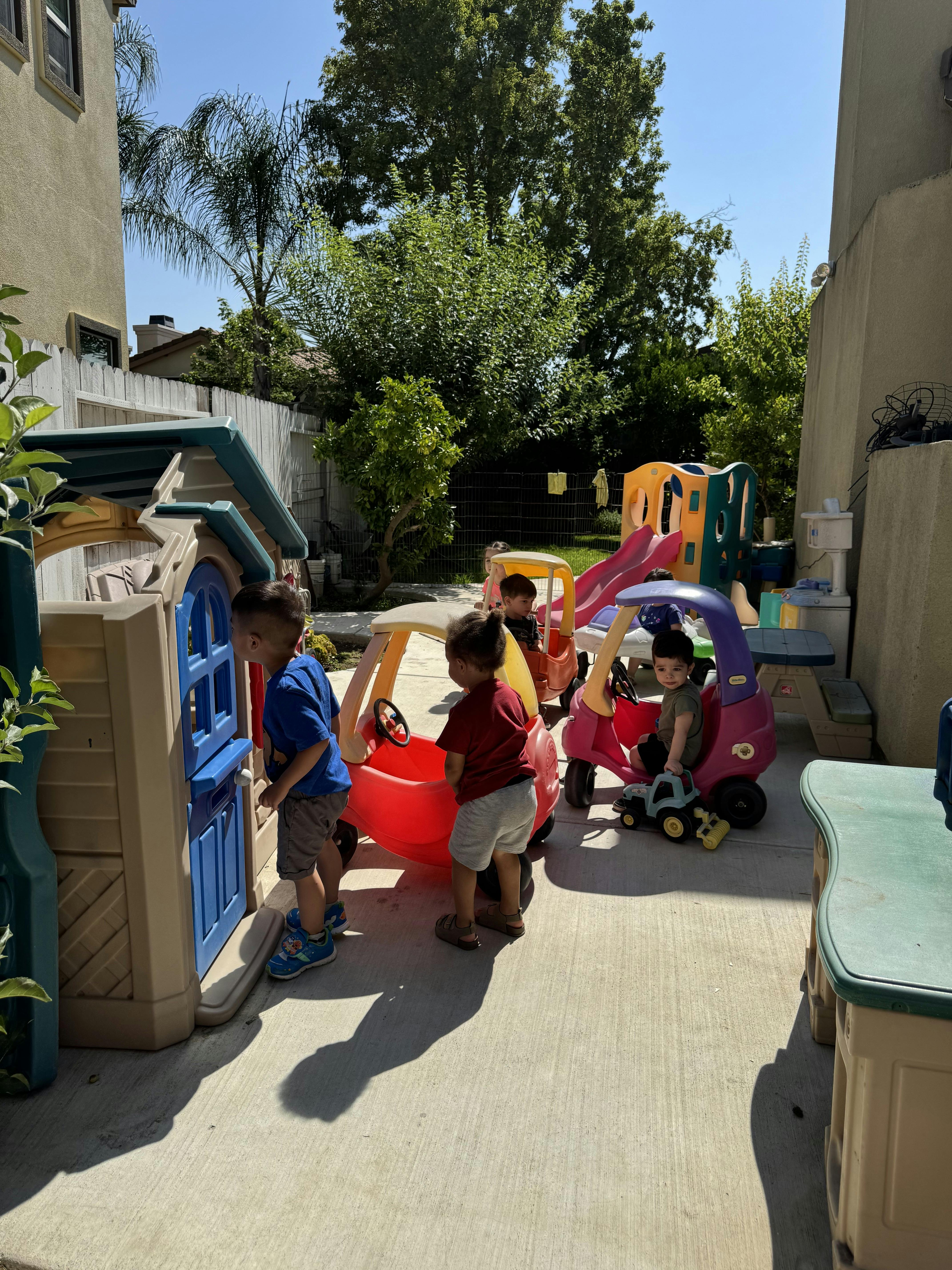 Children playing with toy cars and a playhouse in a backyard