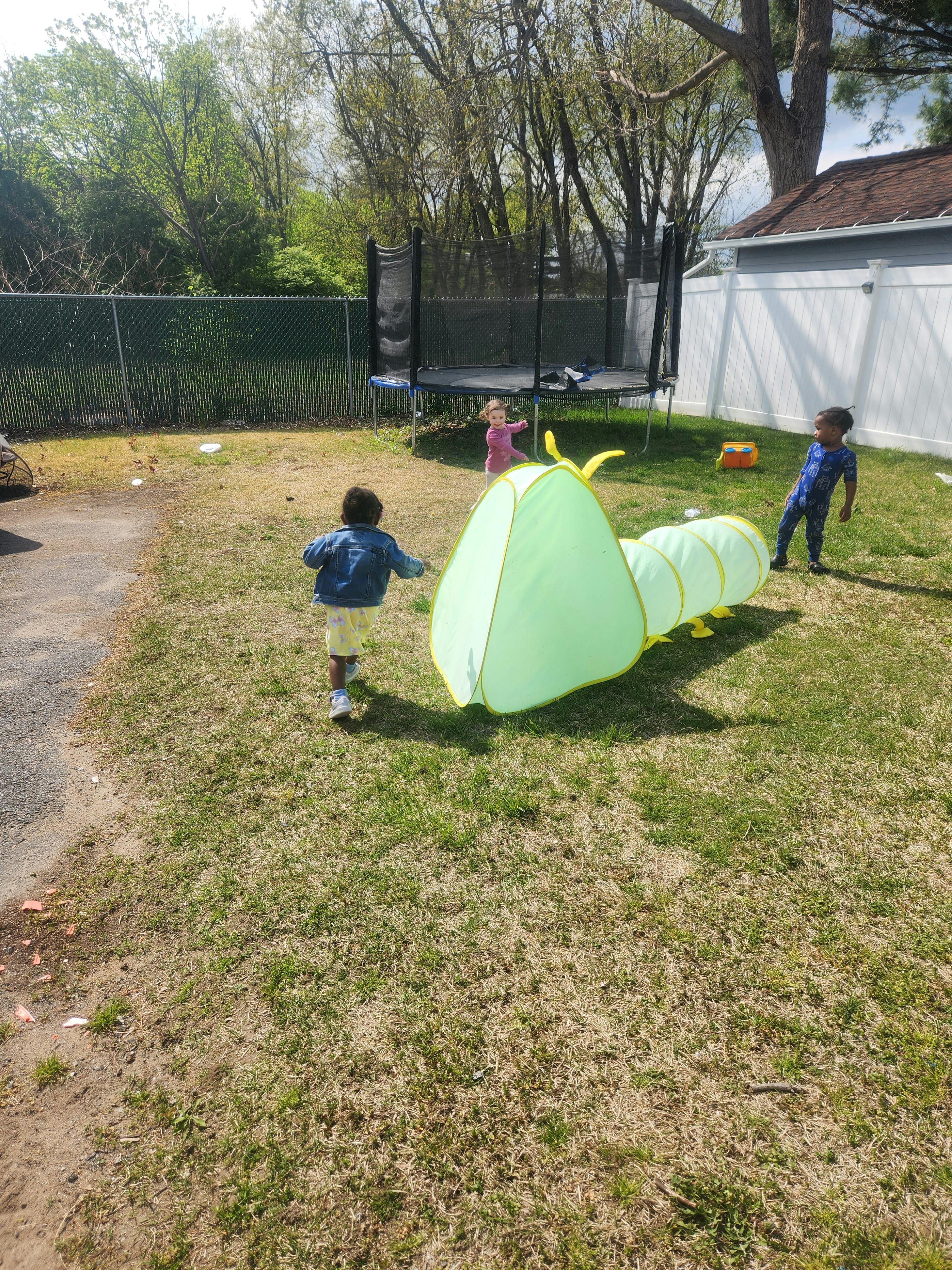 Three children playing in a yard with a green tunnel