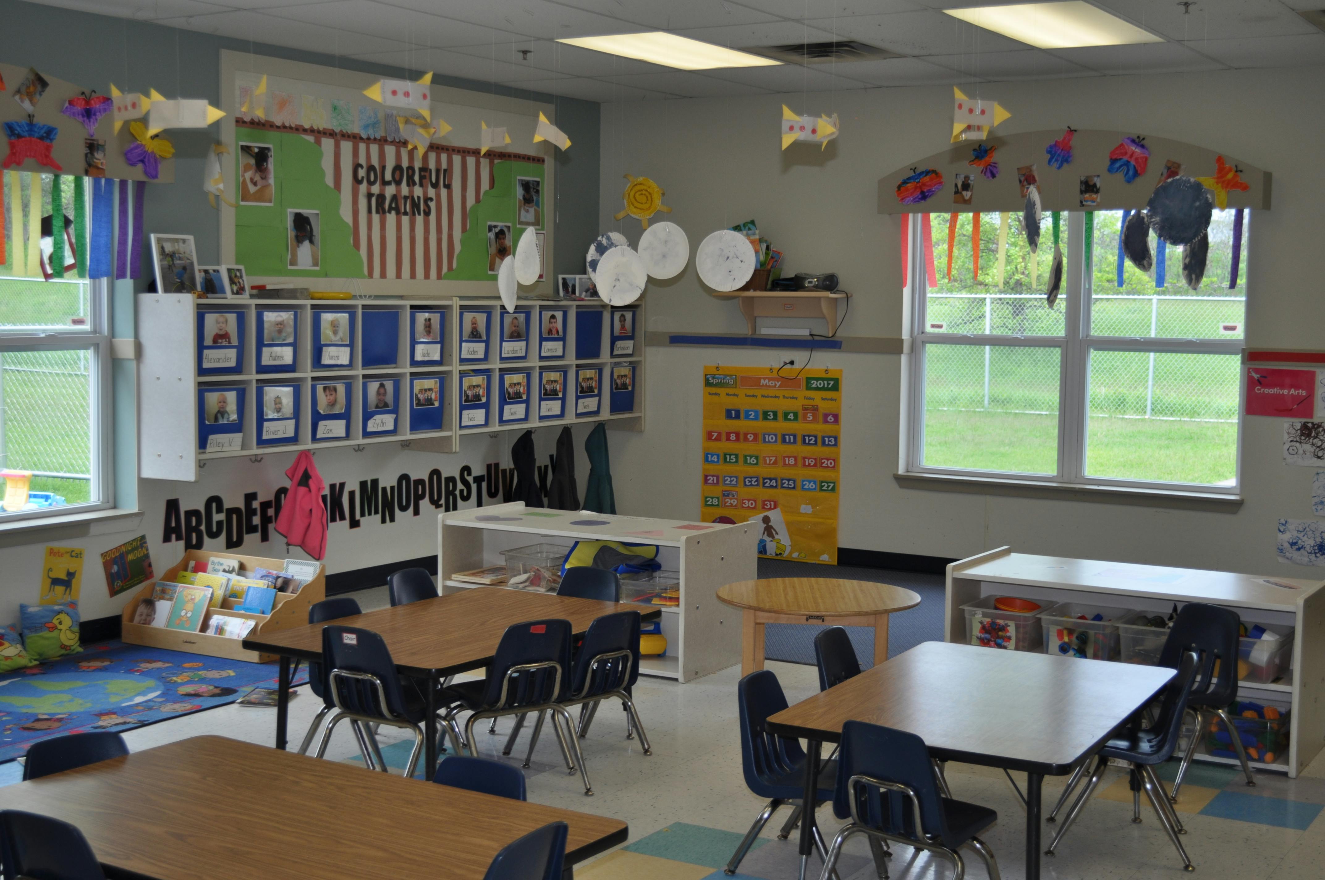 Empty classroom with small tables and chairs, a bulletin board, and a calendar
