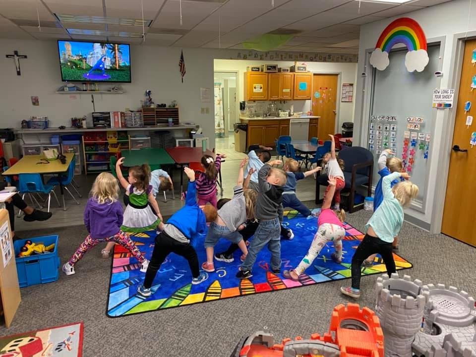 Children doing yoga poses on a colorful mat in a classroom