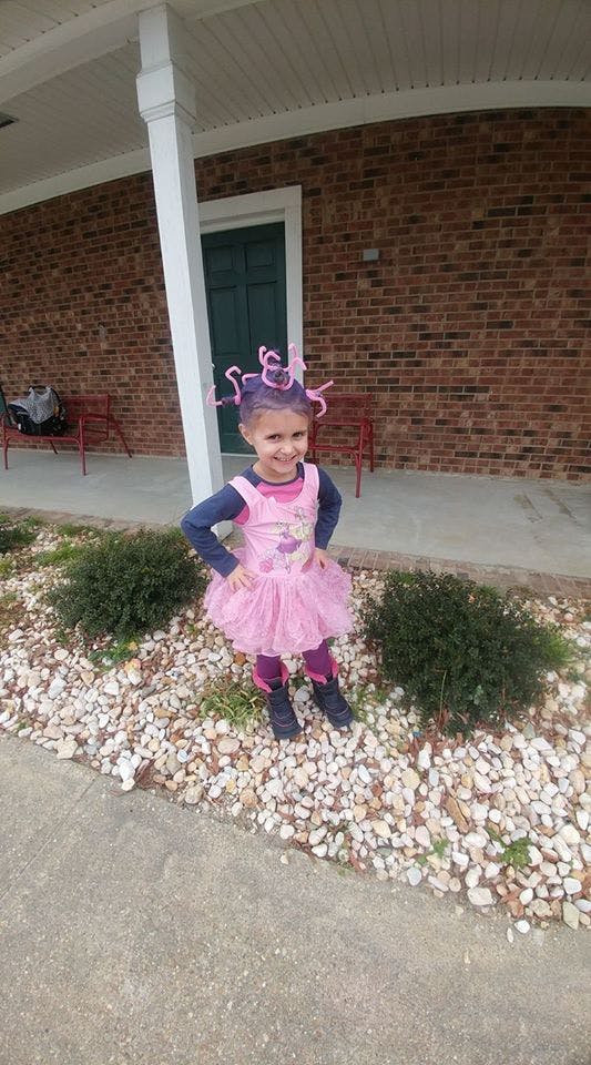 Child in a pink dress with purple hair accessories standing outdoors
