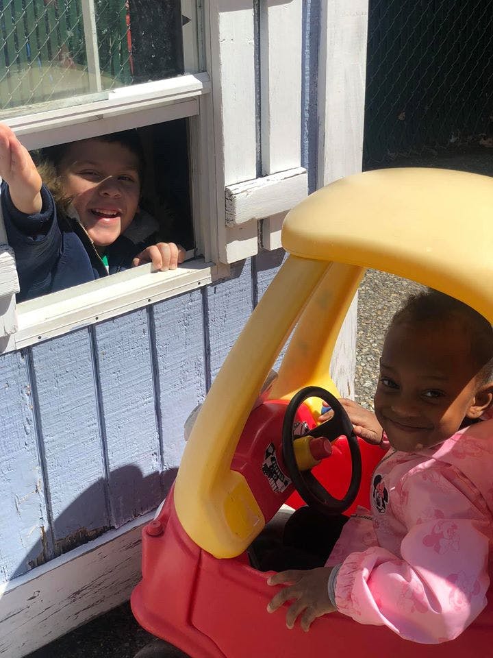 Child in a toy car and a person looking out a window