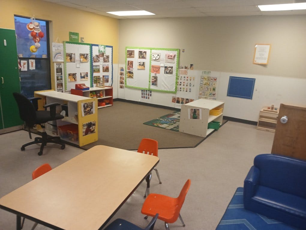 Empty classroom with small tables, chairs, and learning displays on walls