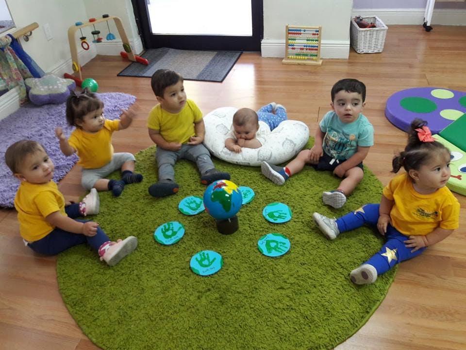 Multiple children sitting on a green rug around a globe