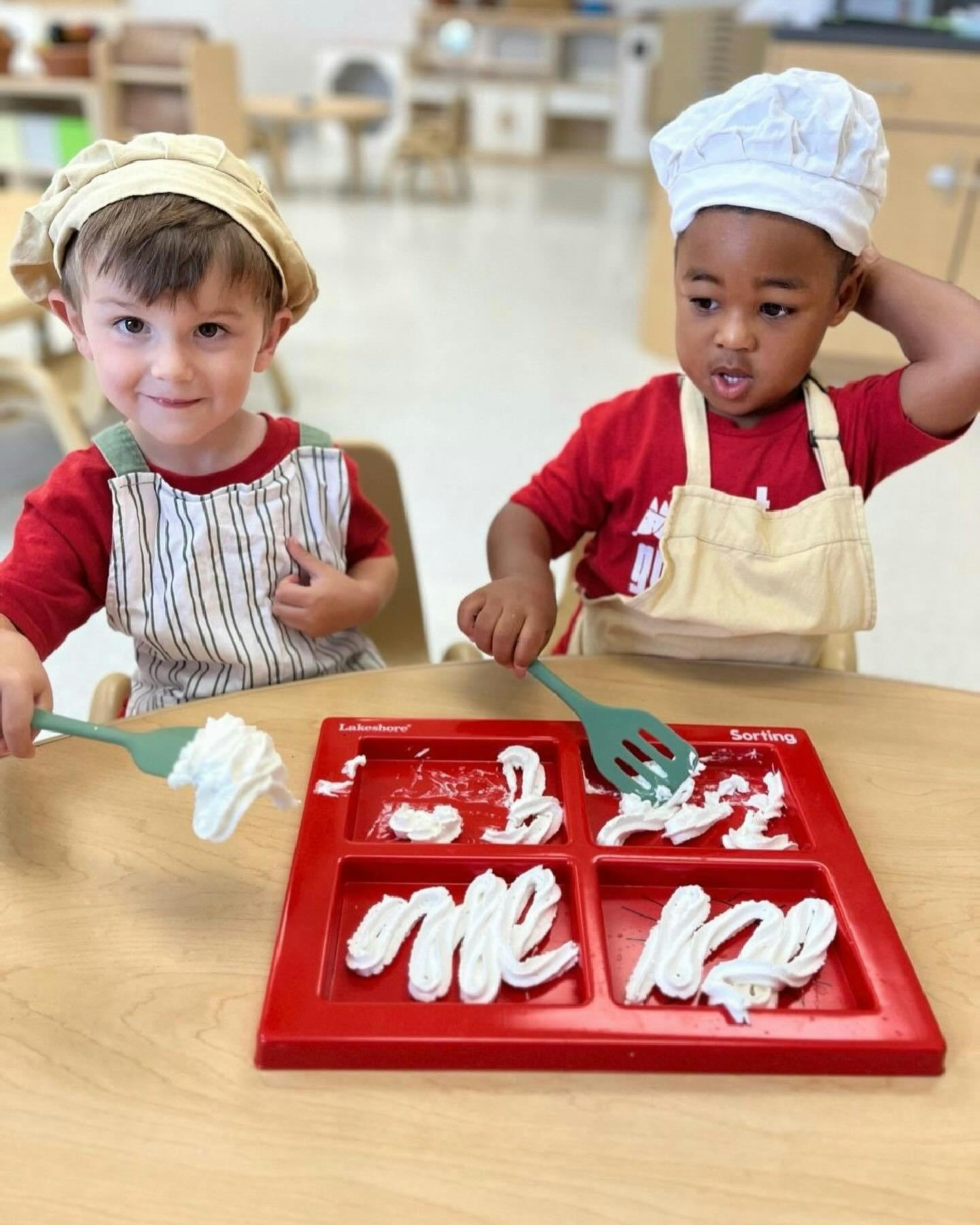 Two children in chef hats and aprons playing with whipped cream