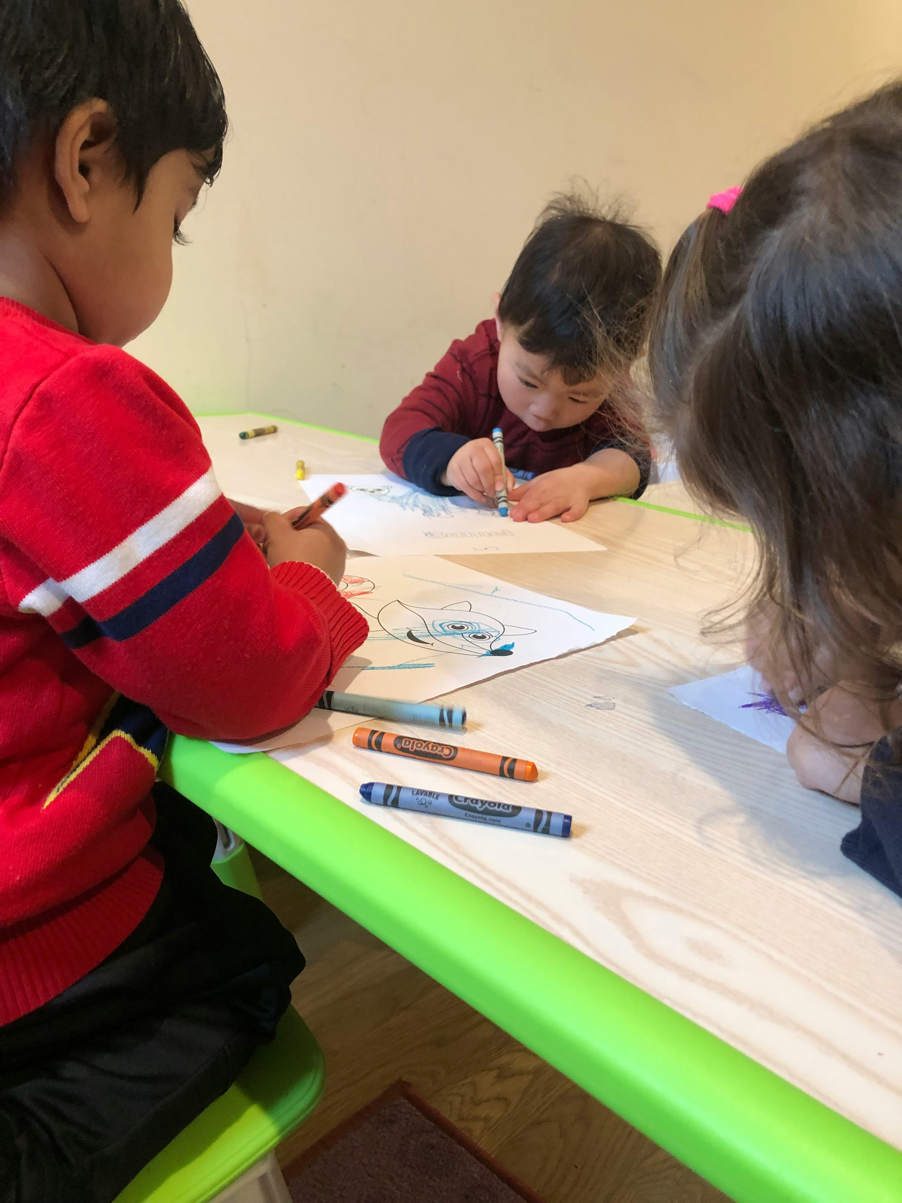 Three children drawing with crayons at a table