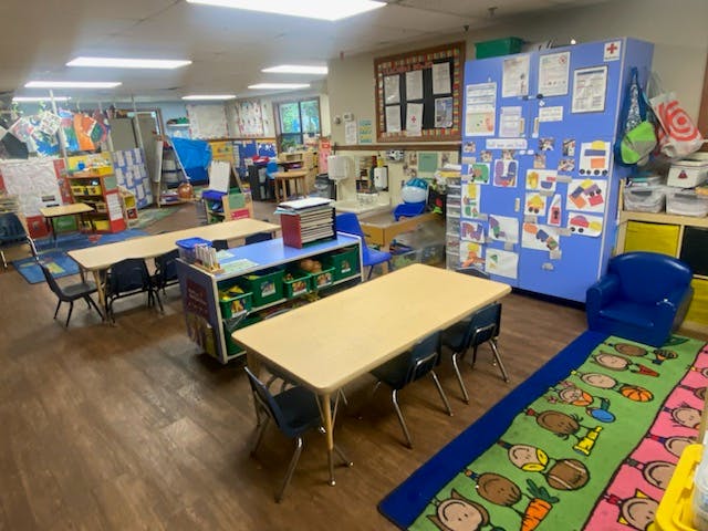 Classroom with child-sized tables and chairs, colorful rugs, and artwork on walls