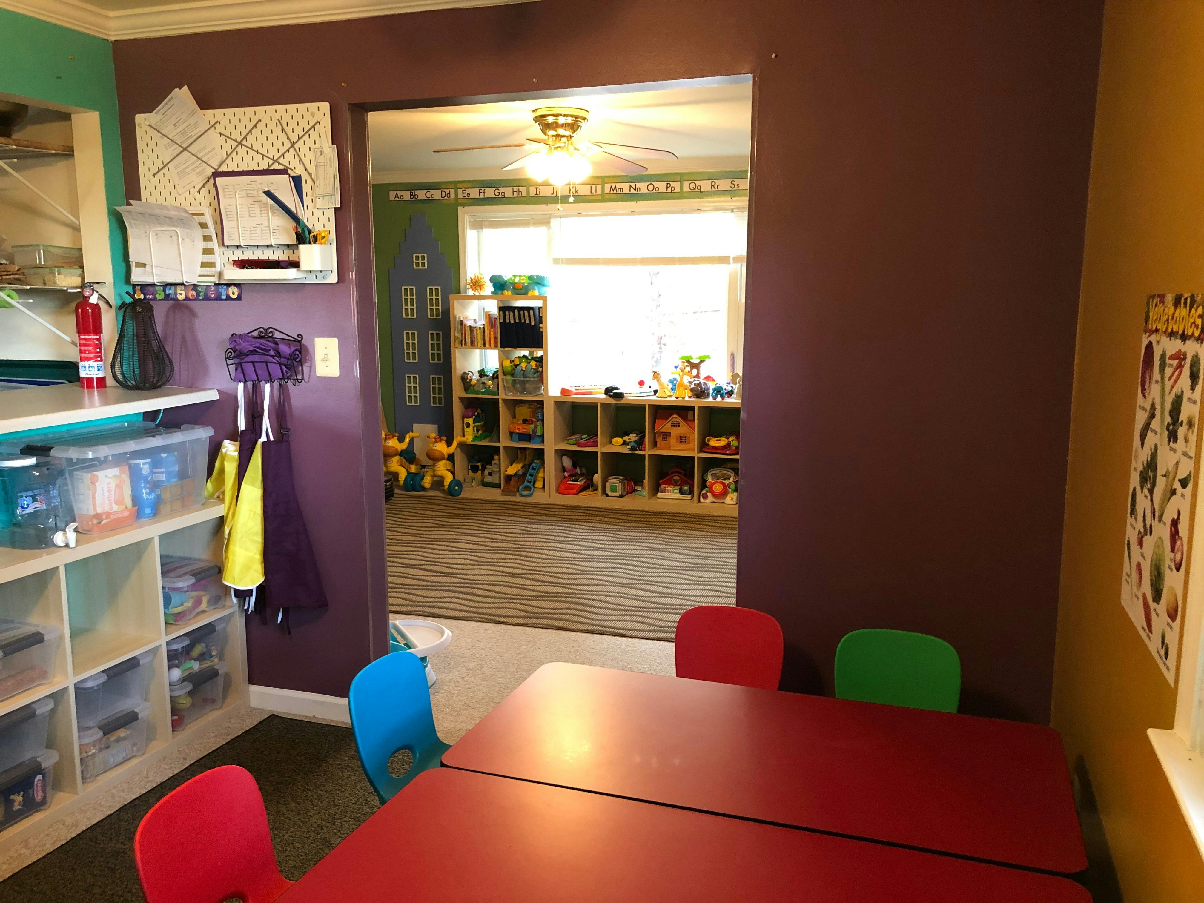Playroom with red tables and colorful chairs, shelves of toys in background