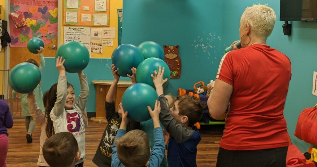 Adult leading children holding up green balls in a room
