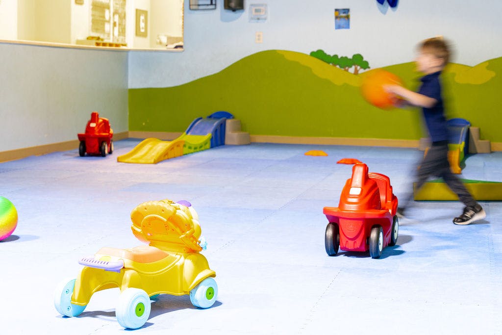 Child running with a ball in a playroom with toys