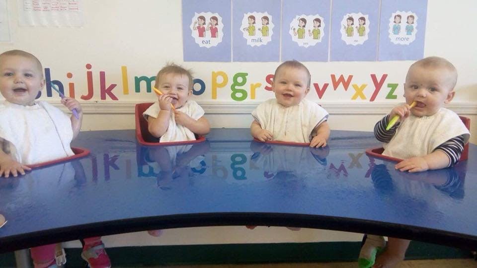 Four babies sitting at a blue table in a classroom