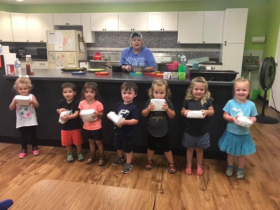 Adult and children holding white objects in a kitchen