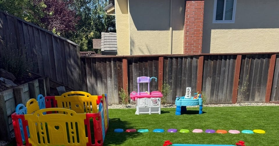 Plastic toy playpen and play kitchen set on a grassy backyard lawn