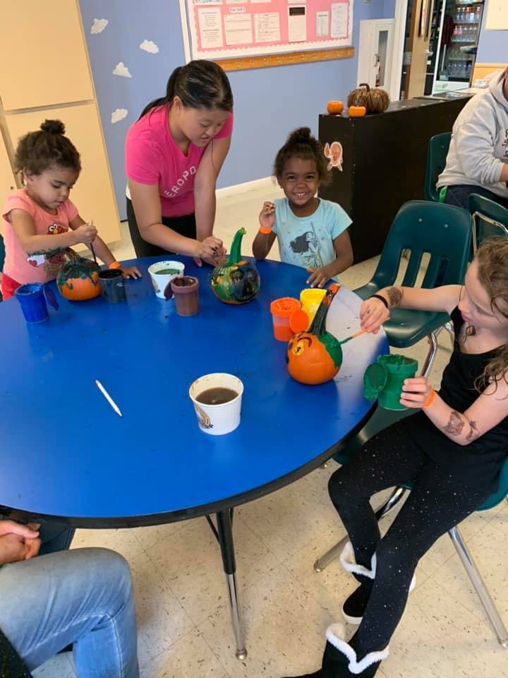 Adult and children painting pumpkins at a blue table