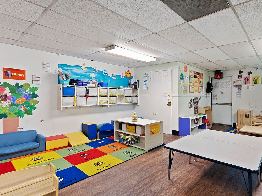 Colorful preschool classroom with cubbies, tables, and a rug