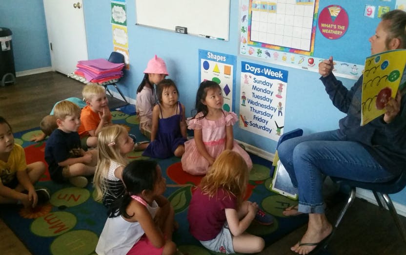Adult reading a book to a group of children in a classroom