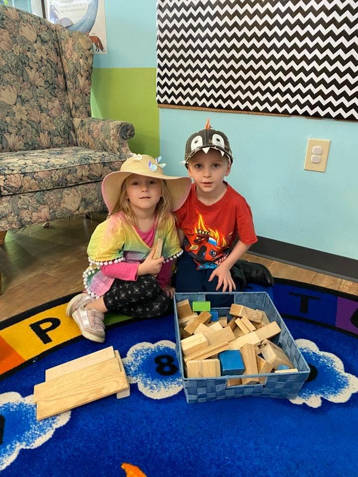 Two children sitting on a rug with a box of building blocks
