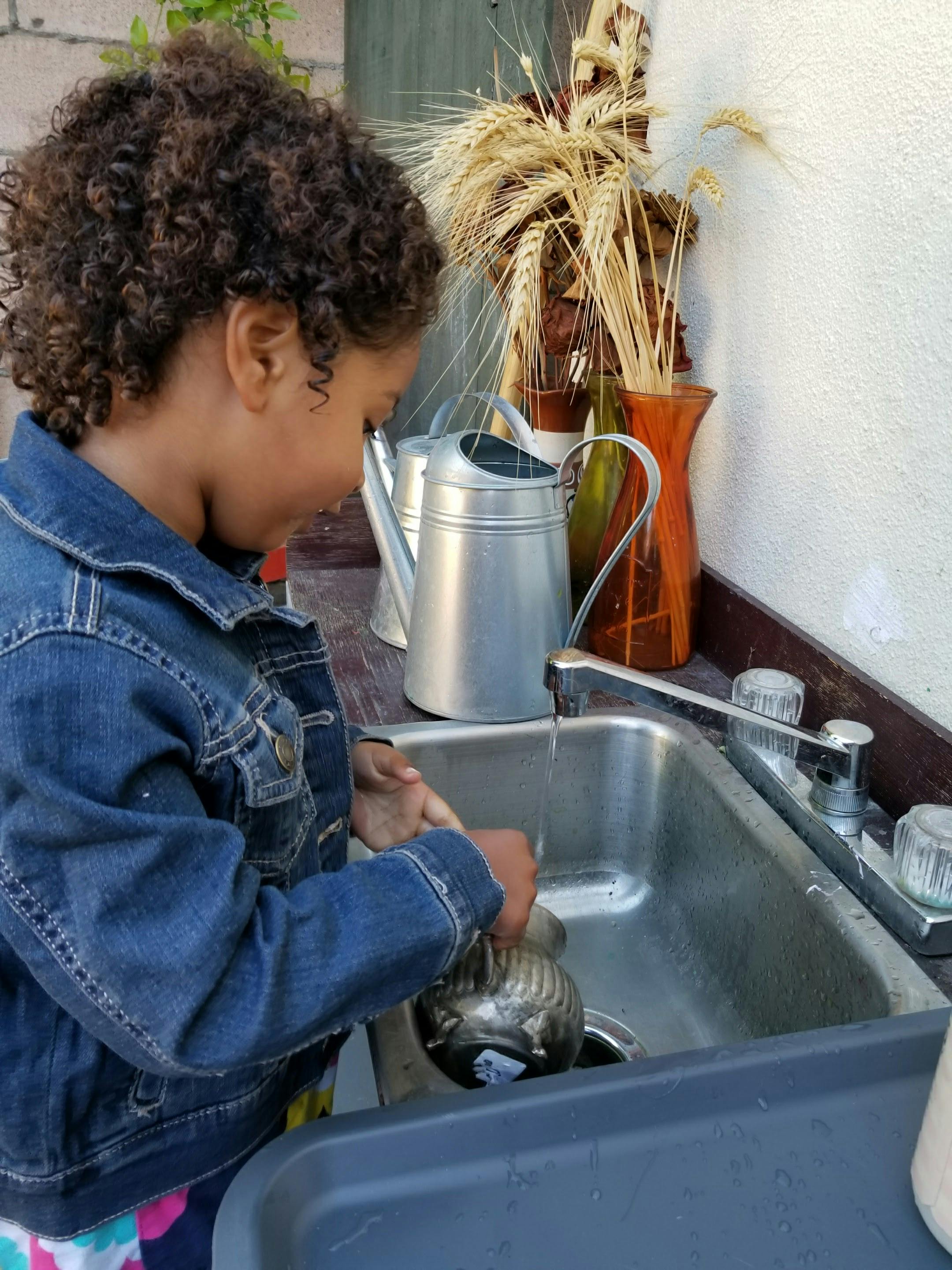 Child washing a metal pot in a sink