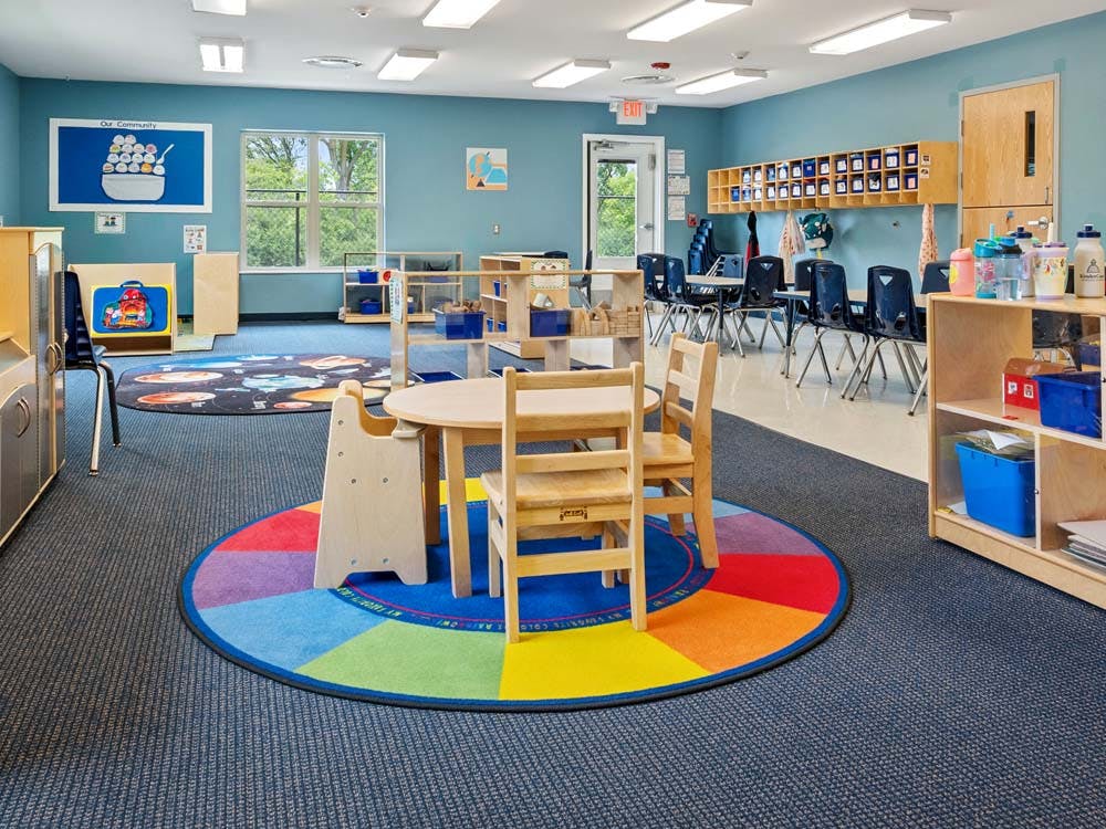 Classroom with blue walls, small wooden tables and chairs, and colorful rugs