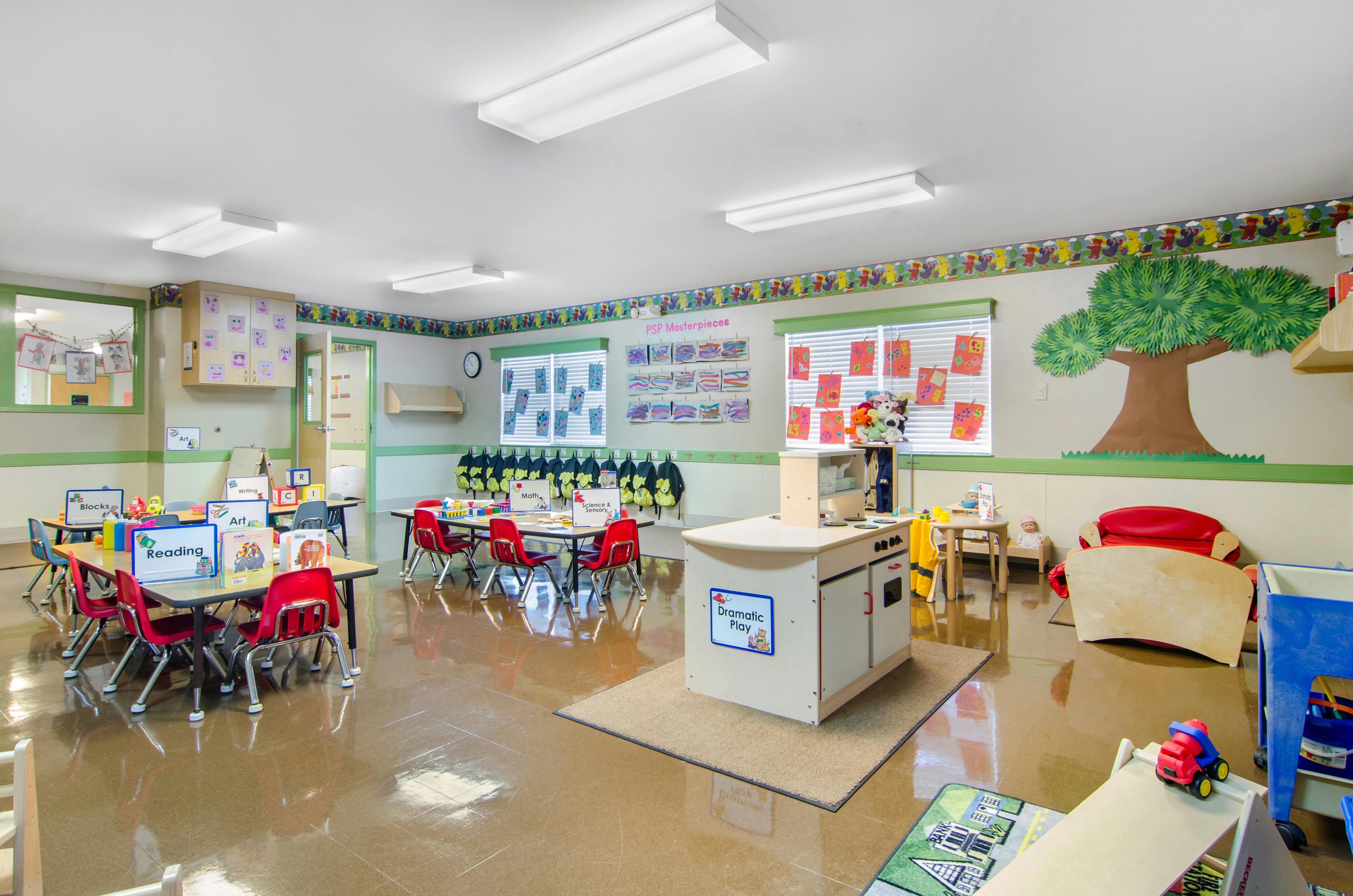 Classroom with small tables and chairs, activity stations, and children's artwork on walls