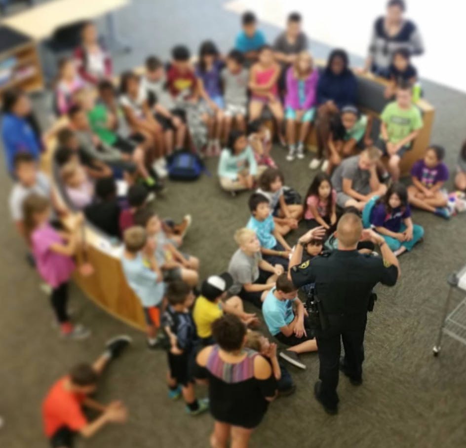 Adult speaking to a group of children and adults sitting on the floor