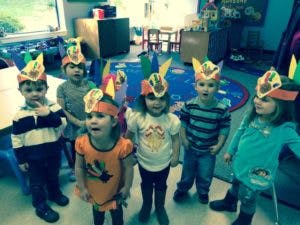 Six children wearing paper headbands with feathers in a classroom