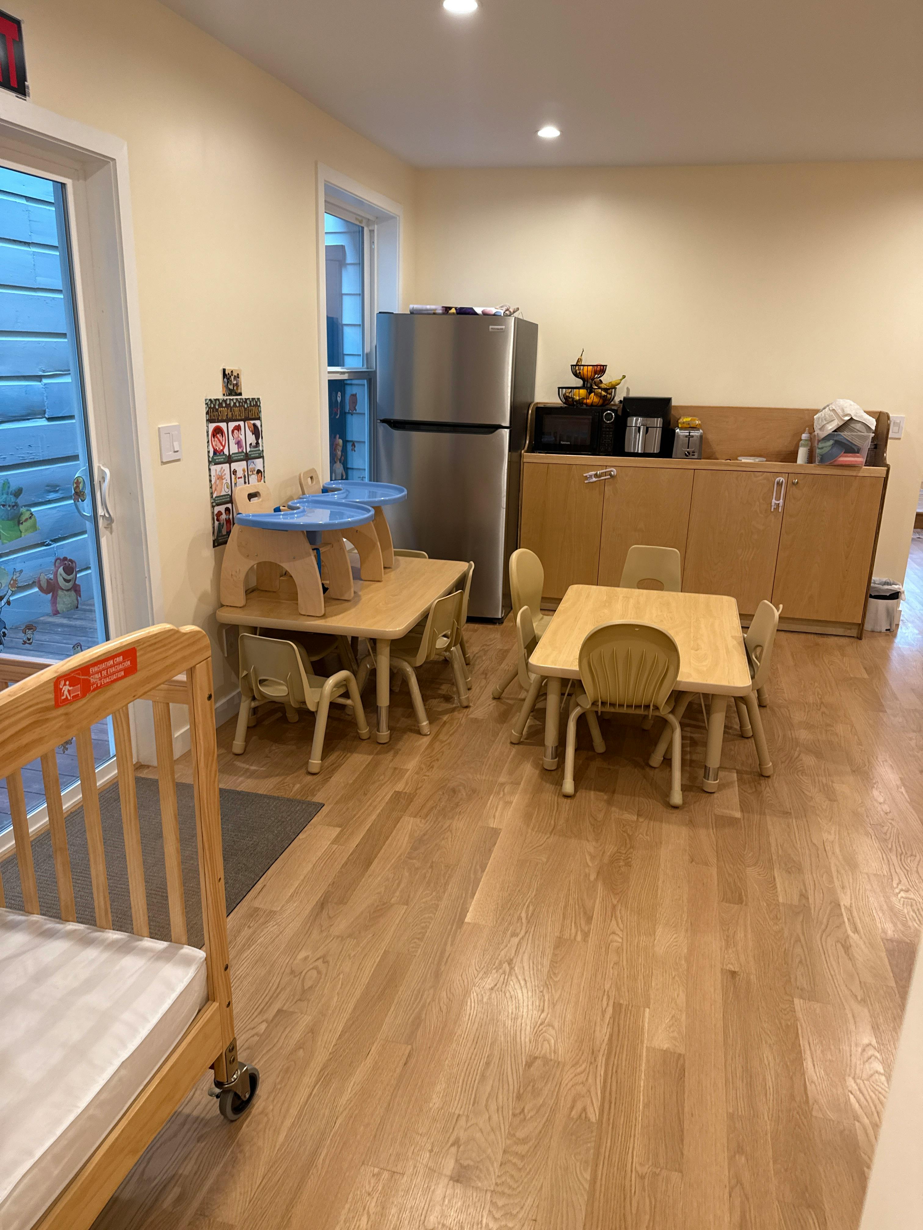 Classroom with small tables and chairs, a crib, and kitchen appliances