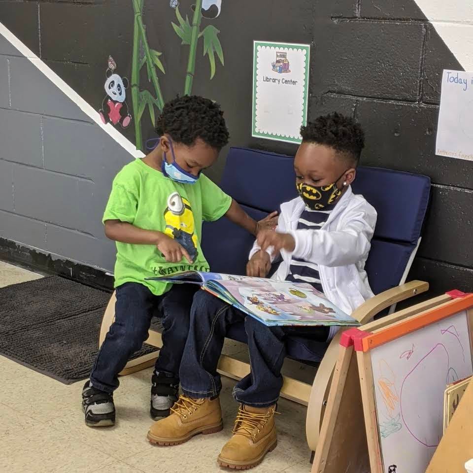 Two children wearing face masks reading a book together