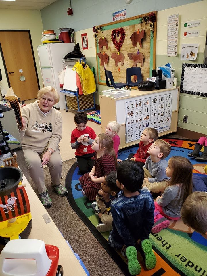 Adult reading a book to a group of children in a classroom