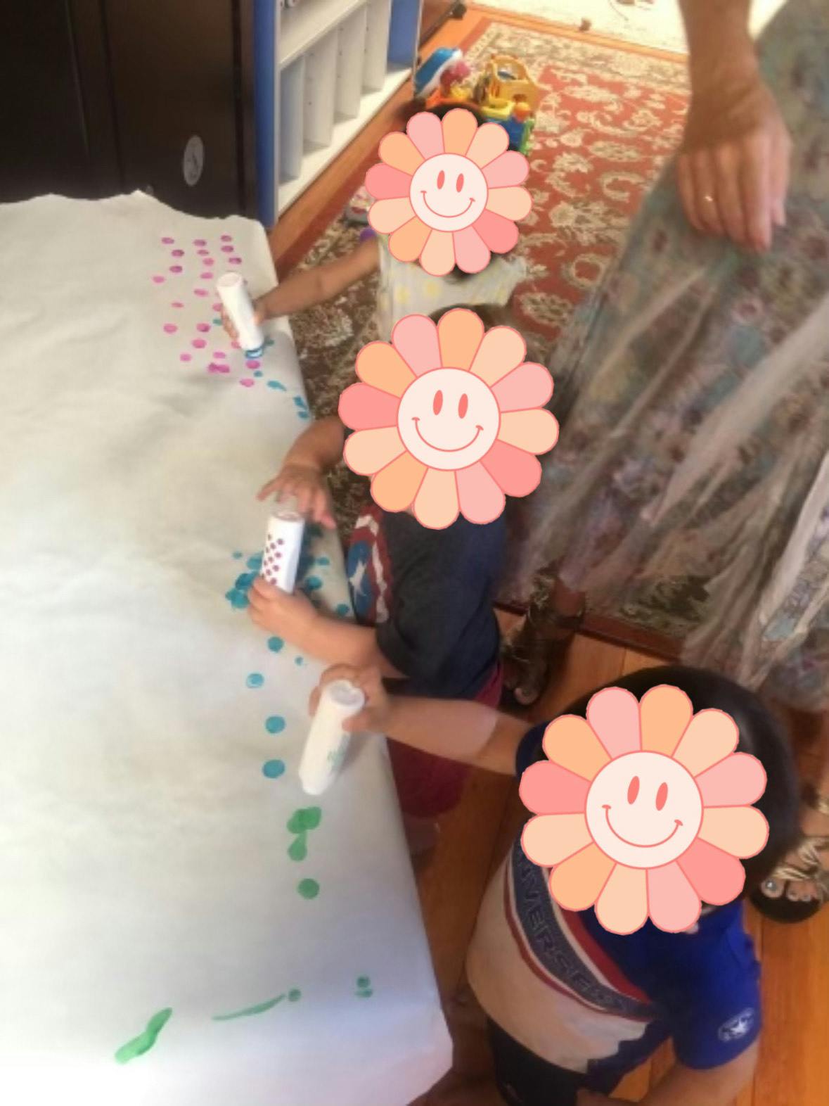 Children painting on a large sheet of paper with dot markers
