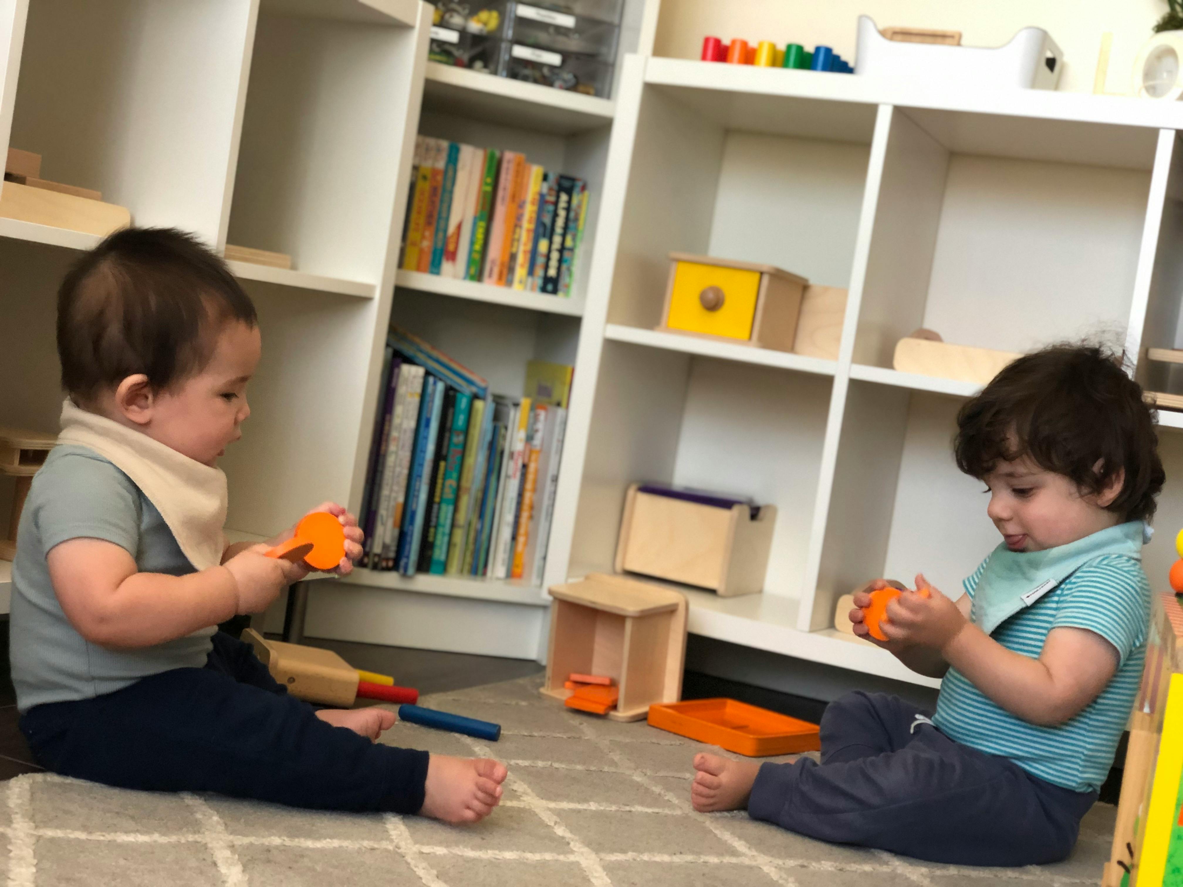 Two children sitting on a rug playing with toys in a classroom