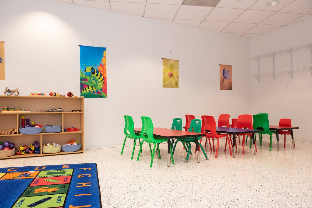 Children's classroom with small tables and chairs, a play rug, and storage shelves