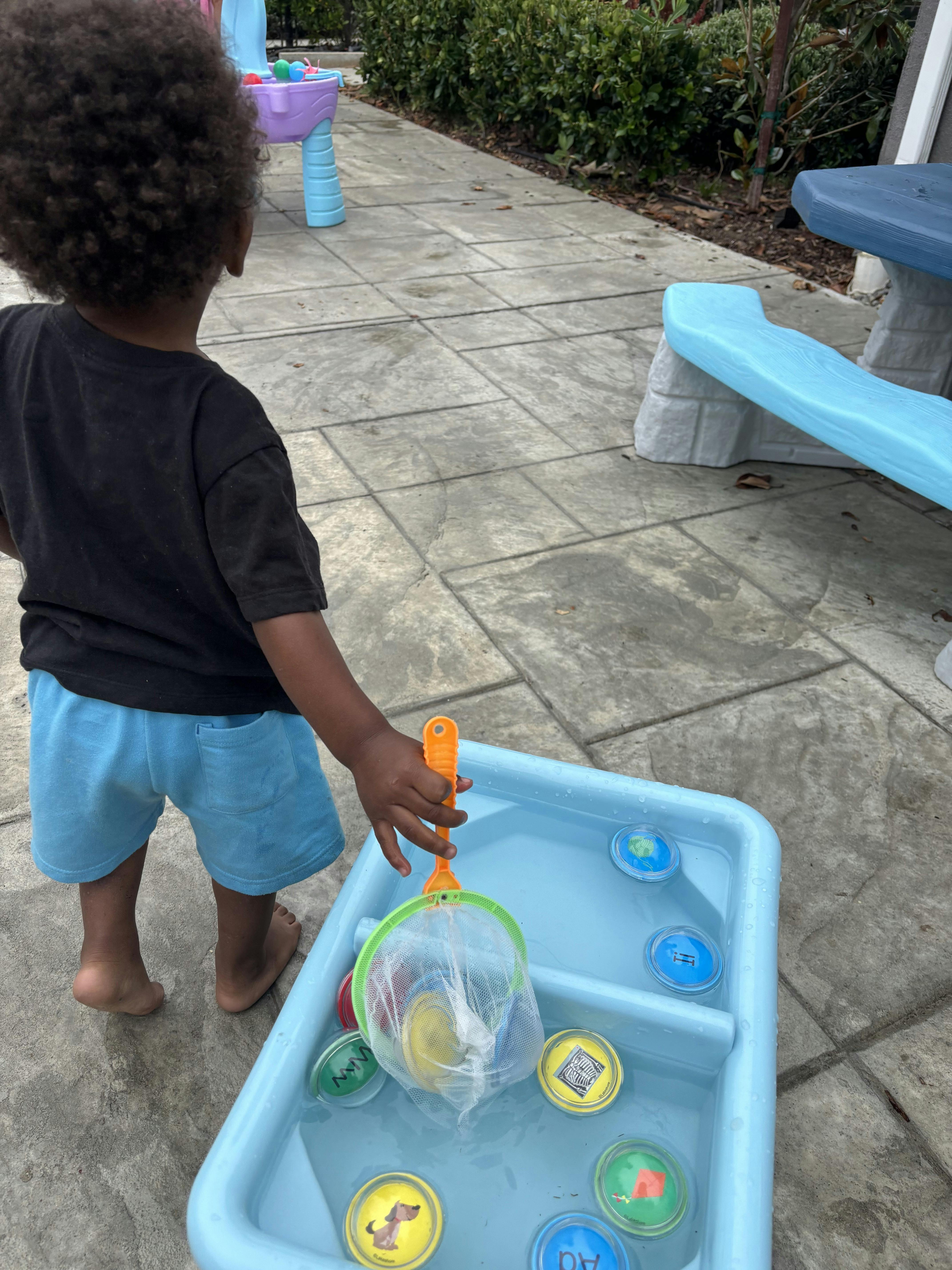 Child playing with a water table and net, fishing for colorful disks