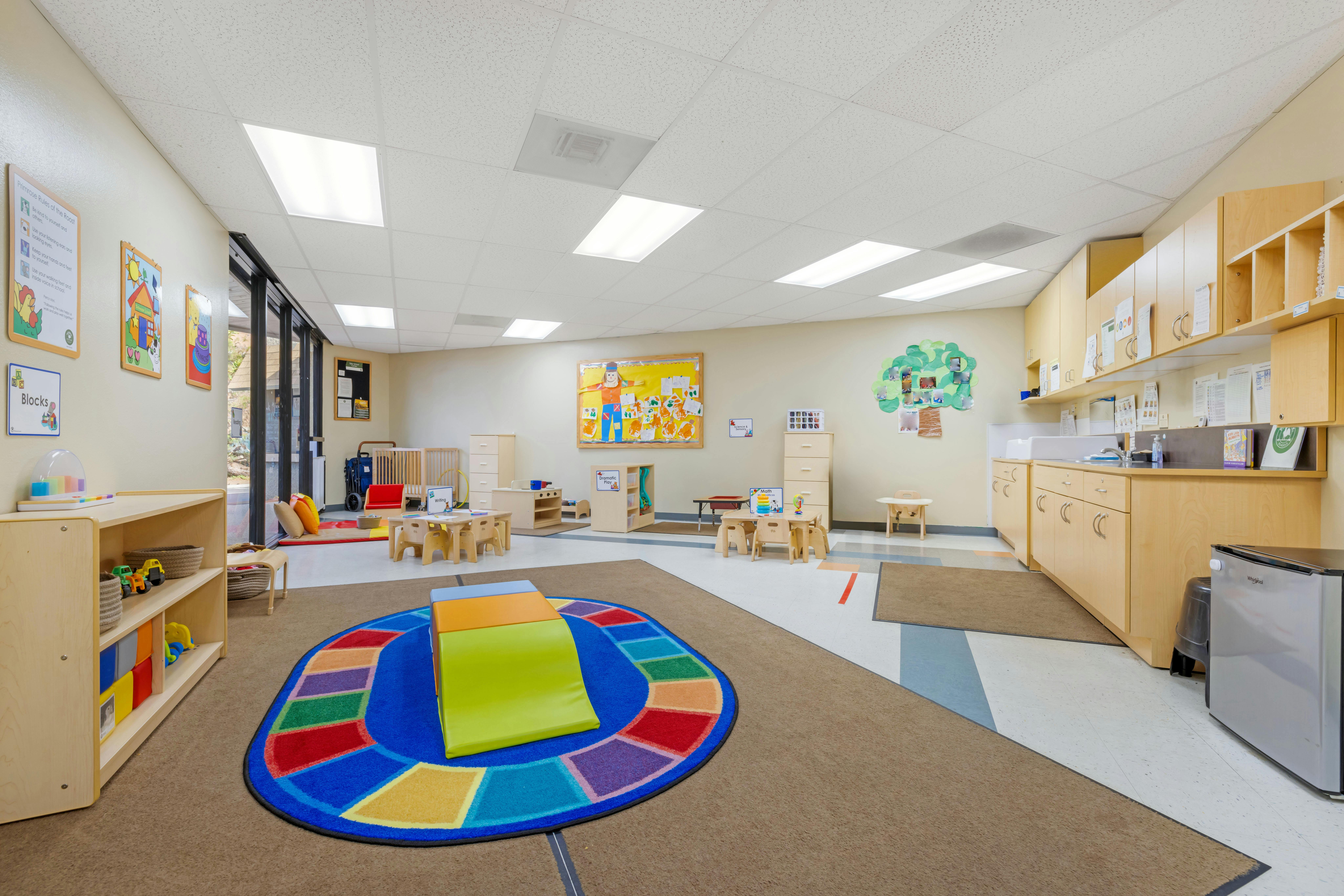 An empty early childhood classroom with small tables and chairs, and play areas