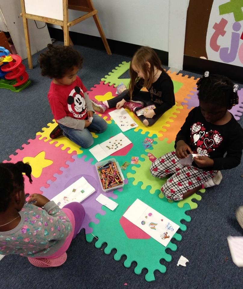 Four children sitting on a colorful mat, engaged in an activity with papers and papers