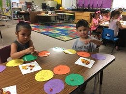 Two children at a table with colorful paper plates and craft supplies