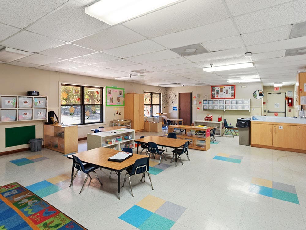 Empty classroom with small tables and chairs, shelves, and windows