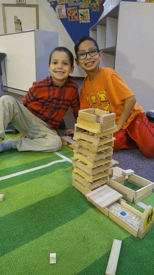 Two children sitting on a green carpet next to wooden blocks