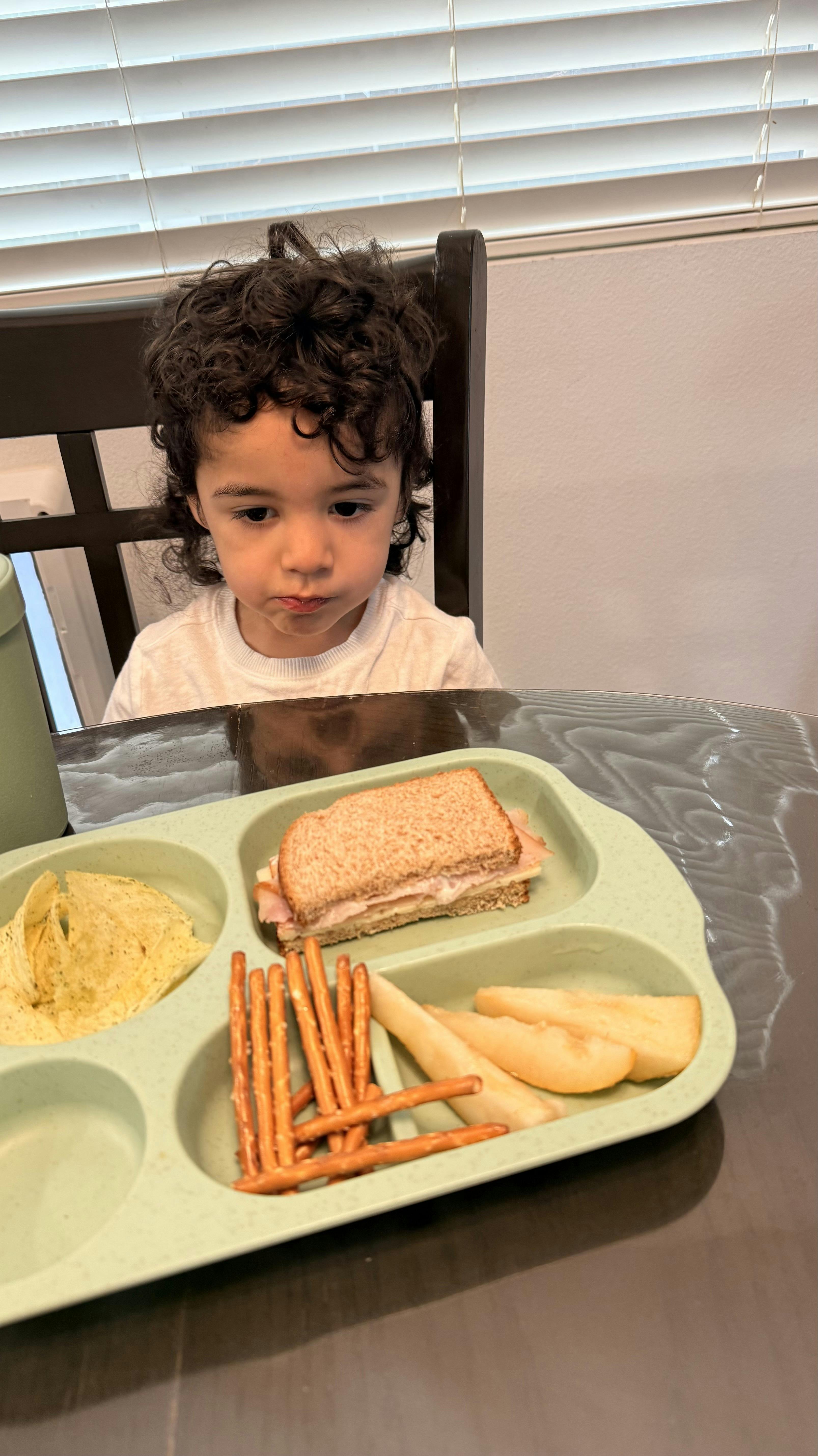 Child sitting at a table with a tray of food including a sandwich and snacks