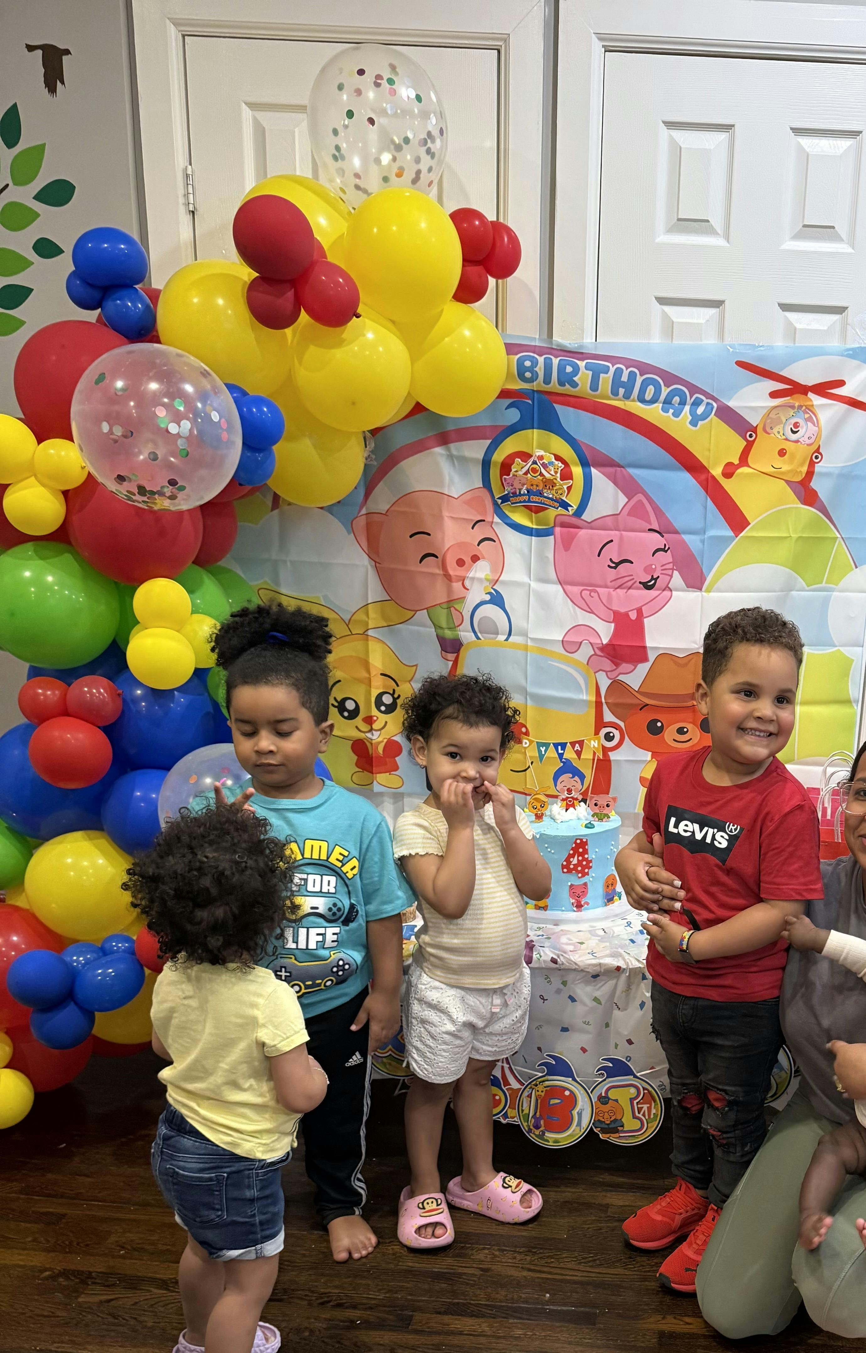 Children standing in front of a birthday banner and balloons